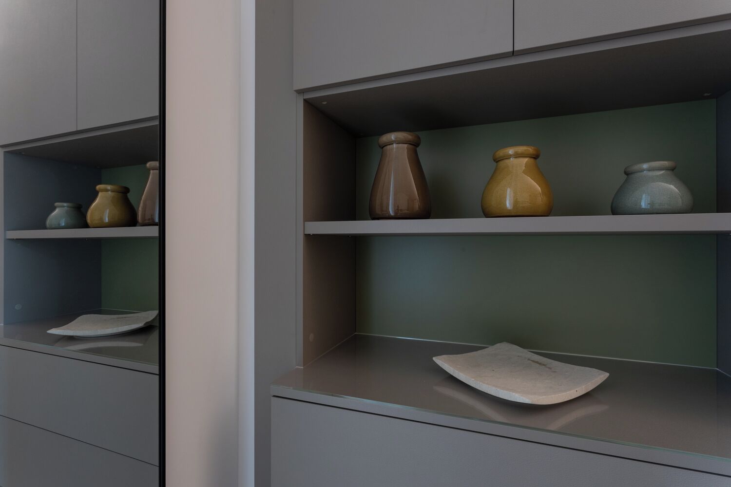 Een modern interieur met grijze kasten en planken waarop keramieken vazen staan.