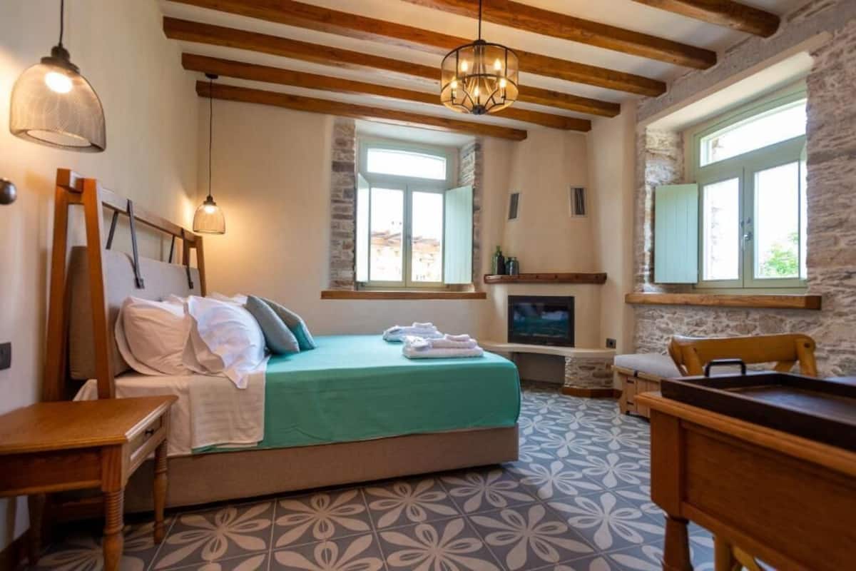 A bedroom with a bed, wooden beams, stone walls, a fireplace, and a television.