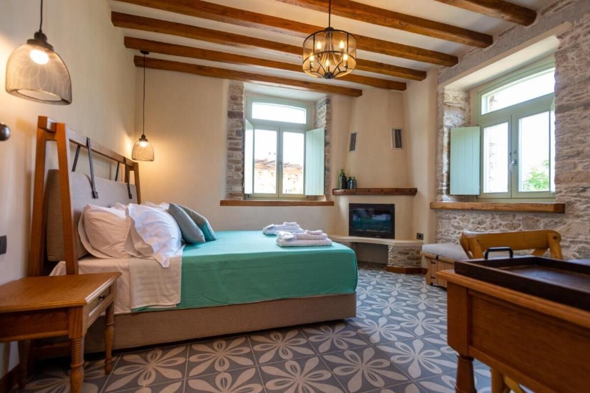 A bedroom with a bed, wooden beams, stone walls, a fireplace, and a television.