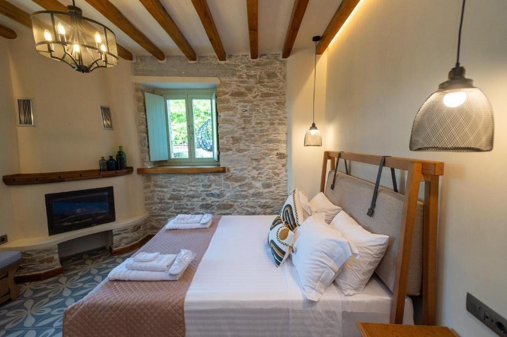 A bedroom with a stone wall, wooden beams, a bed with white bedding, a TV, and a window with a view.