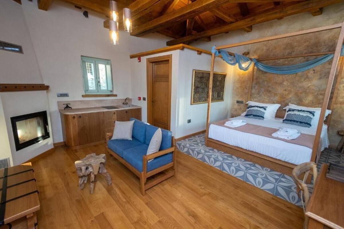 A room with a bed, a sofa, a fireplace, a wooden ceiling, and a window.