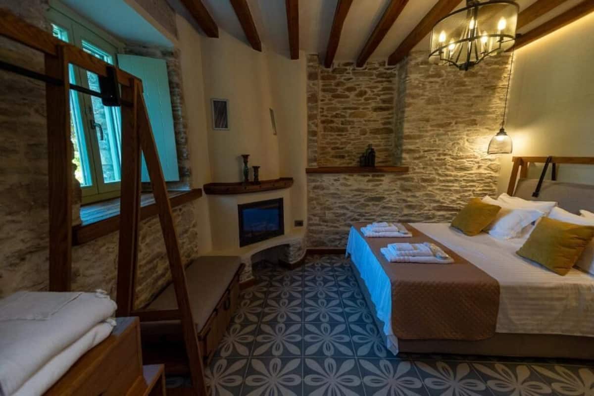 A bedroom with a bed, a wooden ladder, a stone wall, a fireplace, and a chandelier.