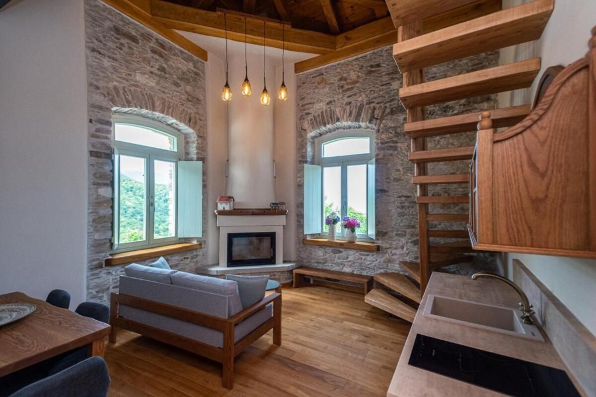 A rustic interior with stone walls, wooden furniture, a fireplace, and a built-in wooden shelf.