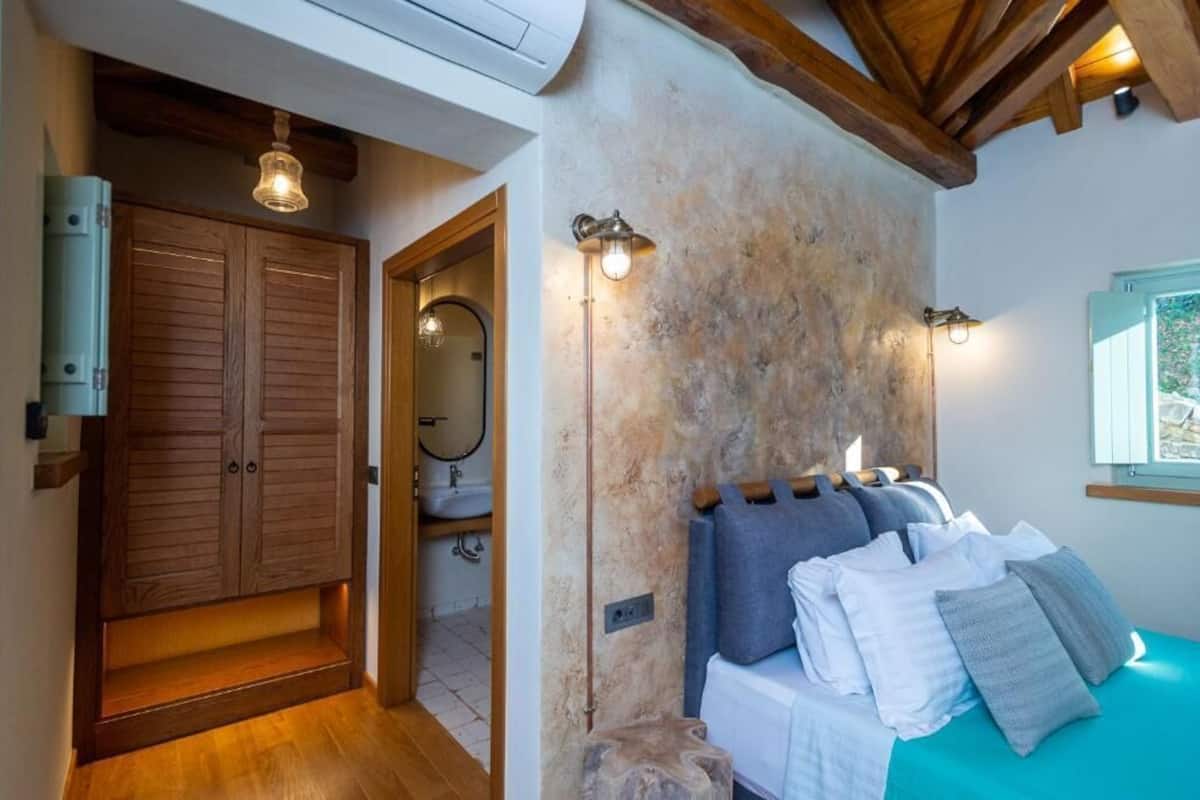 A bedroom with a bed, wooden wardrobe, and a bathroom with a sink and mirror.