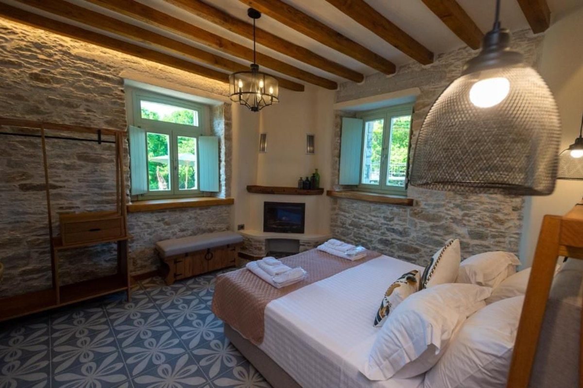 Un dormitorio con paredes de piedra, vigas de madera, una cama grande, un banco y un televisor.