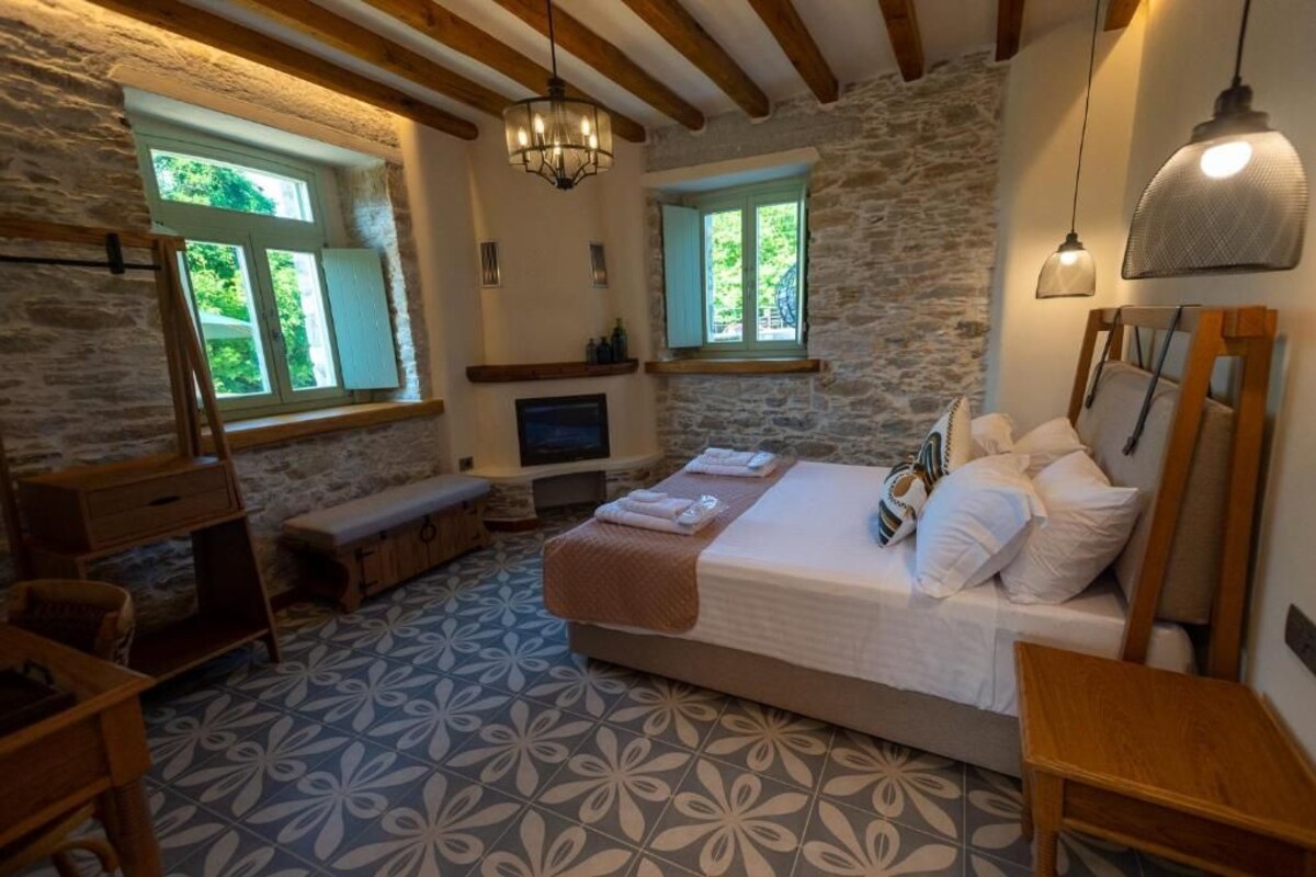 A room with a stone wall, a bed with white bedding, a bench, a wooden table, and a television.