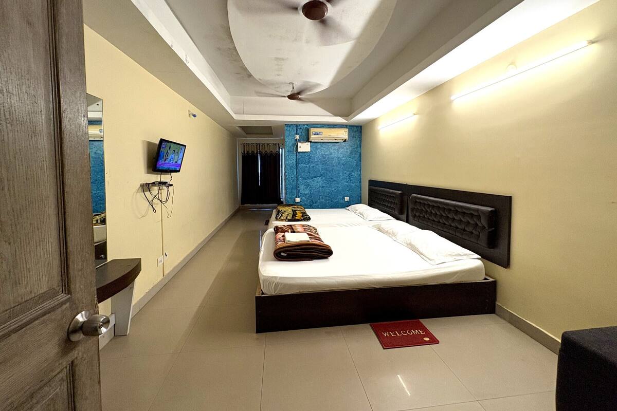 Una habitación de hotel con una cama, televisión, ventilador de techo y felpudo.