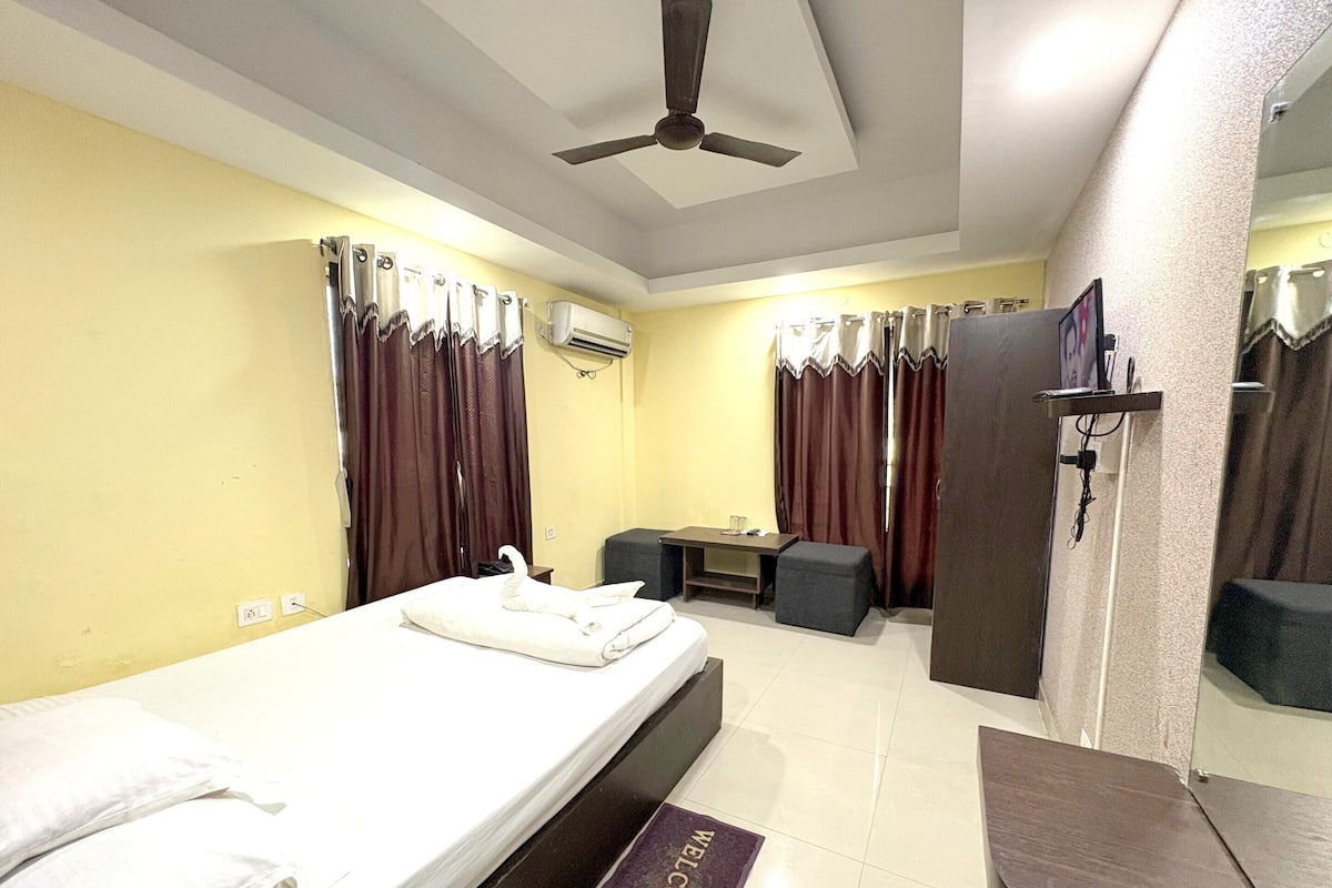 Una habitación de hotel con cama, escritorio, silla, mesita, espejo y puerta.