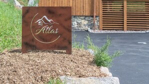 A wooden cabin with a balcony, a stone wall, and a sign with the name 'Atlas.' - ✨ Chalet Atlas – Hot Tub, Sauna & 500m from the Slopes (Gérardmer)