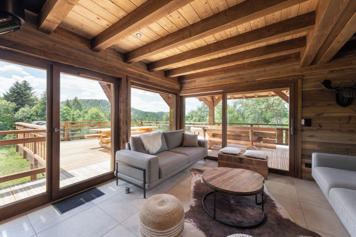 A spacious wooden interior with large windows, a sofa, a coffee table, and a view of a deck and forest.