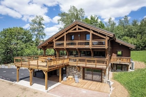 Een houten chalet met twee verdiepingen, een balkon, een stenen fundering en een ruim terras.