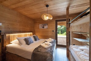 Een houten slaapkamer met een bed, hoofdbord, hanglamp en uitzicht op de natuur.