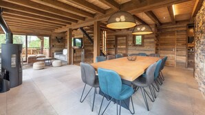 A spacious dining area with a large wooden table and modern chairs, a stone wall, and a fireplace. - ✨ Chalet Atlas – Hot Tub, Sauna & 500m from the Slopes (Gérardmer)