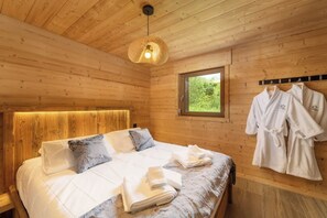 Une chambre aménagée dans une cabane en bois, avec un lit, des oreillers, des serviettes, un luminaire suspendu et une fenêtre.