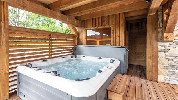 A hot tub in a wooden outdoor area with a stone wall and a wooden bench. - ✨ Chalet Atlas – Hot Tub, Sauna & 500m from the Slopes (Gérardmer)