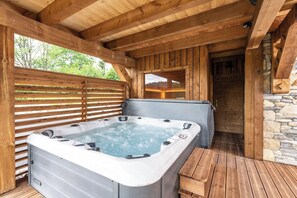 Een hottub in een houten buitenruimte met een stenen muur en een houten bank.