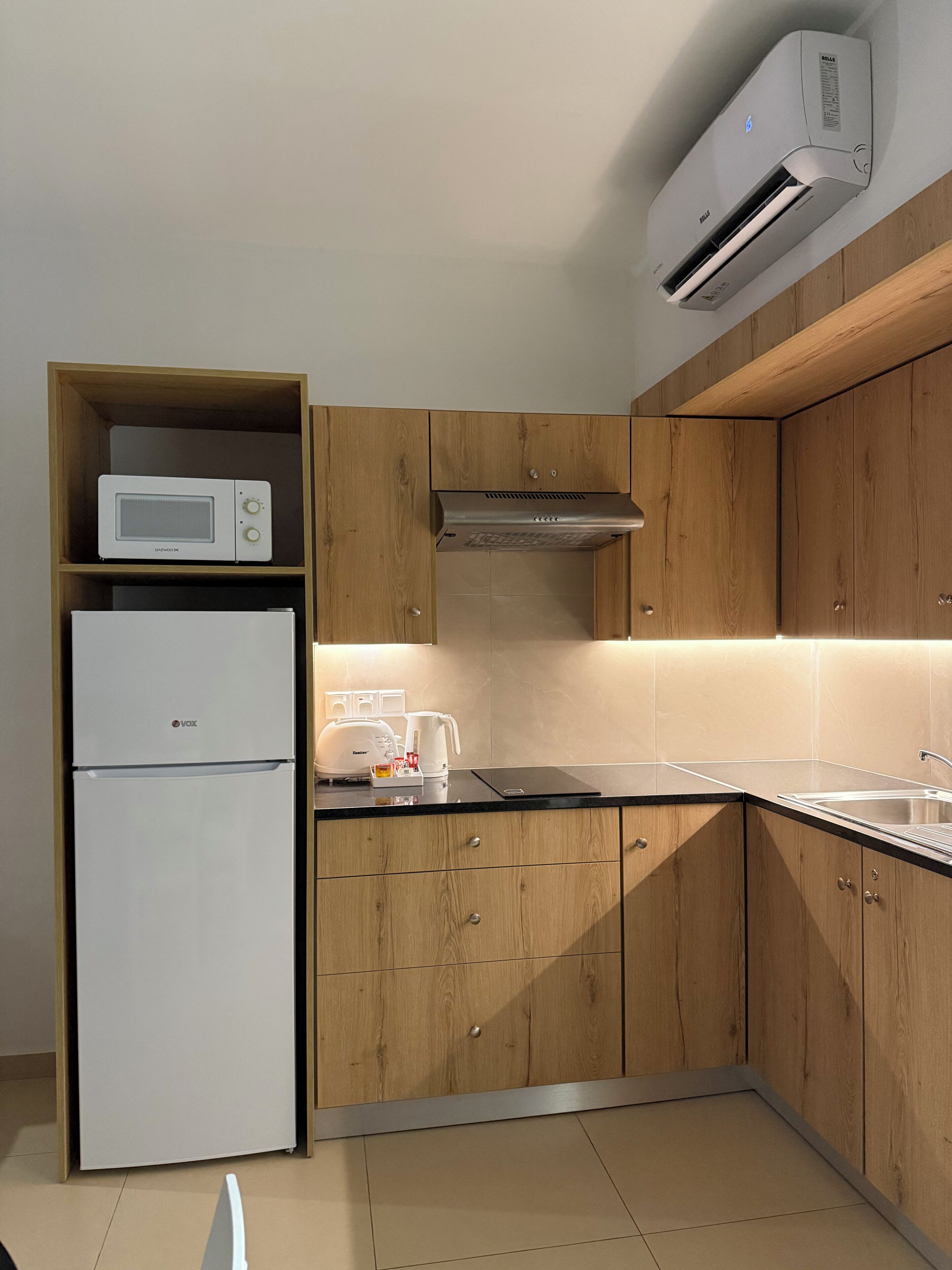 Une cuisine moderne avec des meubles en bois, un réfrigérateur blanc, un four à micro-ondes, un grille-pain et un climatiseur.