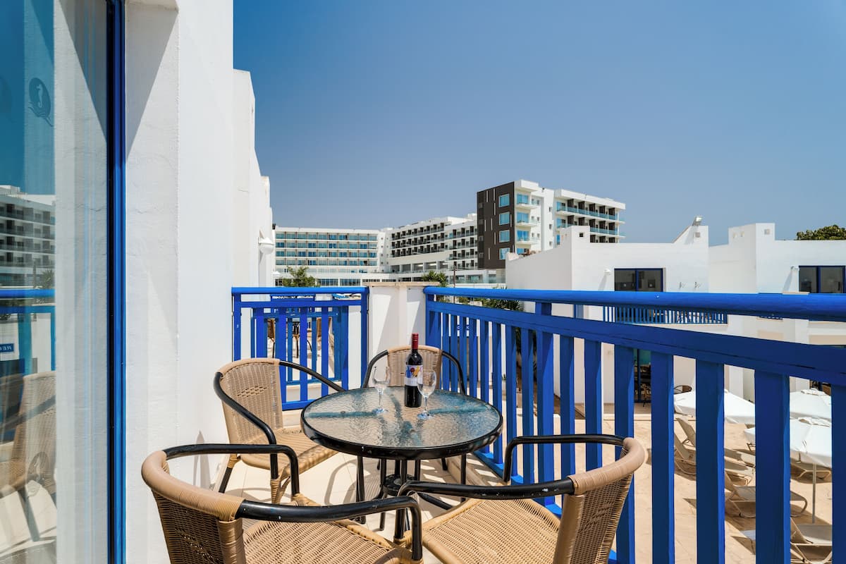 A balcony with wicker chairs and a table, overlooking a cityscape with modern buildings.