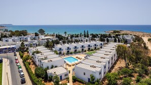 Ein Küstenresort mit mehreren weißen Gebäuden, einem zentralen Poolbereich und Blick auf das Meer.