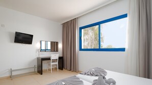 Ein Hotelzimmer mit Bett, Schreibtisch, Stuhl, Fernseher und einem Fenster mit Vorhängen.