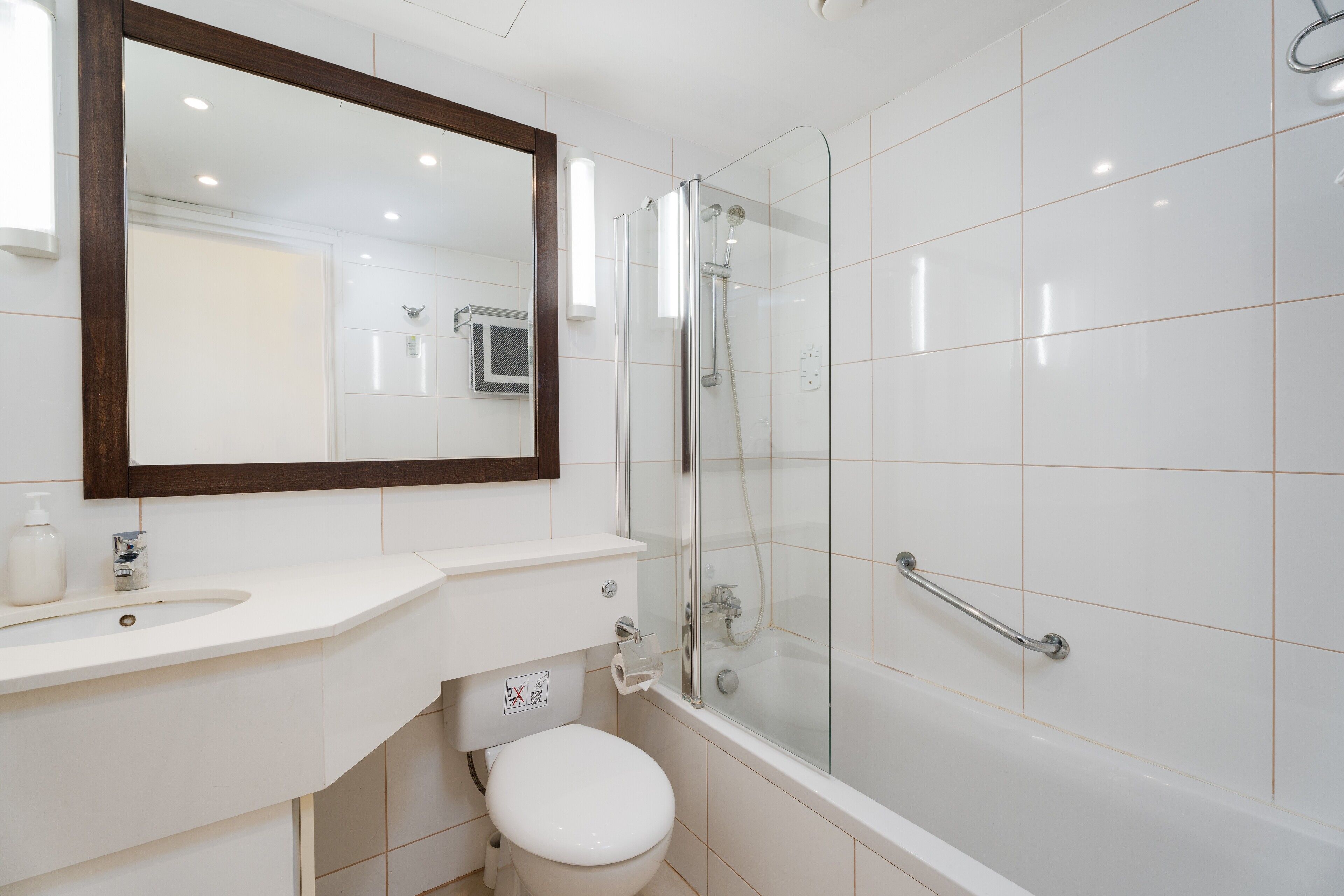 A modern bathroom with a glass-enclosed shower, a white toilet, and a vanity with a mirror.