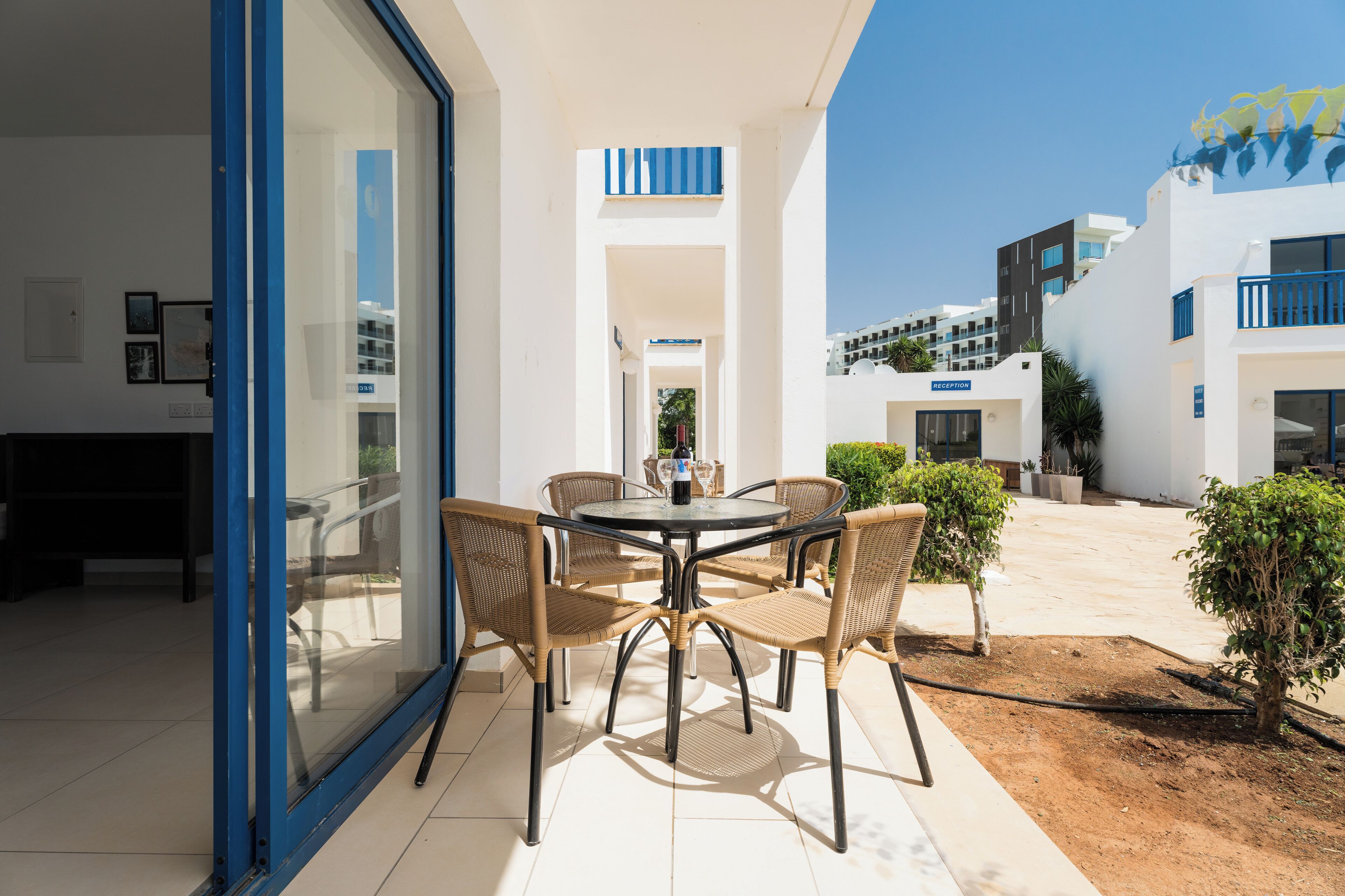 A modern outdoor patio with a round table and wicker chairs, surrounded by a glass door and white walls.