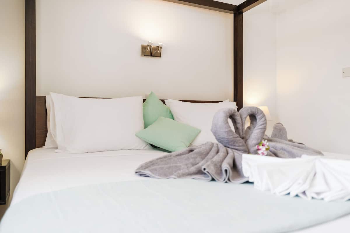 A neatly made bed with white and green pillows, a gray towel, and a small table with a flower.