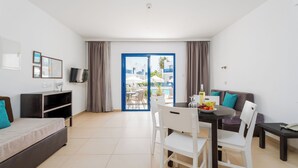 Ein modernes Hotelzimmer mit Balkon, Essbereich, Sofa und Fernseher.