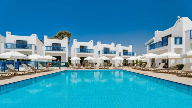 Ein Pool mit Liegestühlen und Sonnenschirmen, umgeben von weißen Gebäuden mit blauen Geländern.