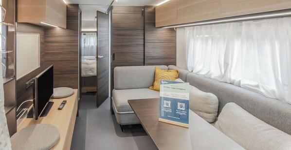 A modern RV interior with a sofa, a table, a TV, and a remote control. - HOTIDAY Lodge Castiglione (Castiglione della Pescaia)