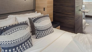 Una habitación de hotel moderna con una cama, almohadas, un armario de madera y una mesita.