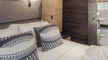 Habitación de hotel moderna con cama, dos almohadas estampadas, una mesita de noche, un armario pequeño y vistas al baño.