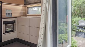 Cocina compacta con electrodomésticos integrados, ventana con vista a zonas verdes y un pequeño espacio exterior con asientos.