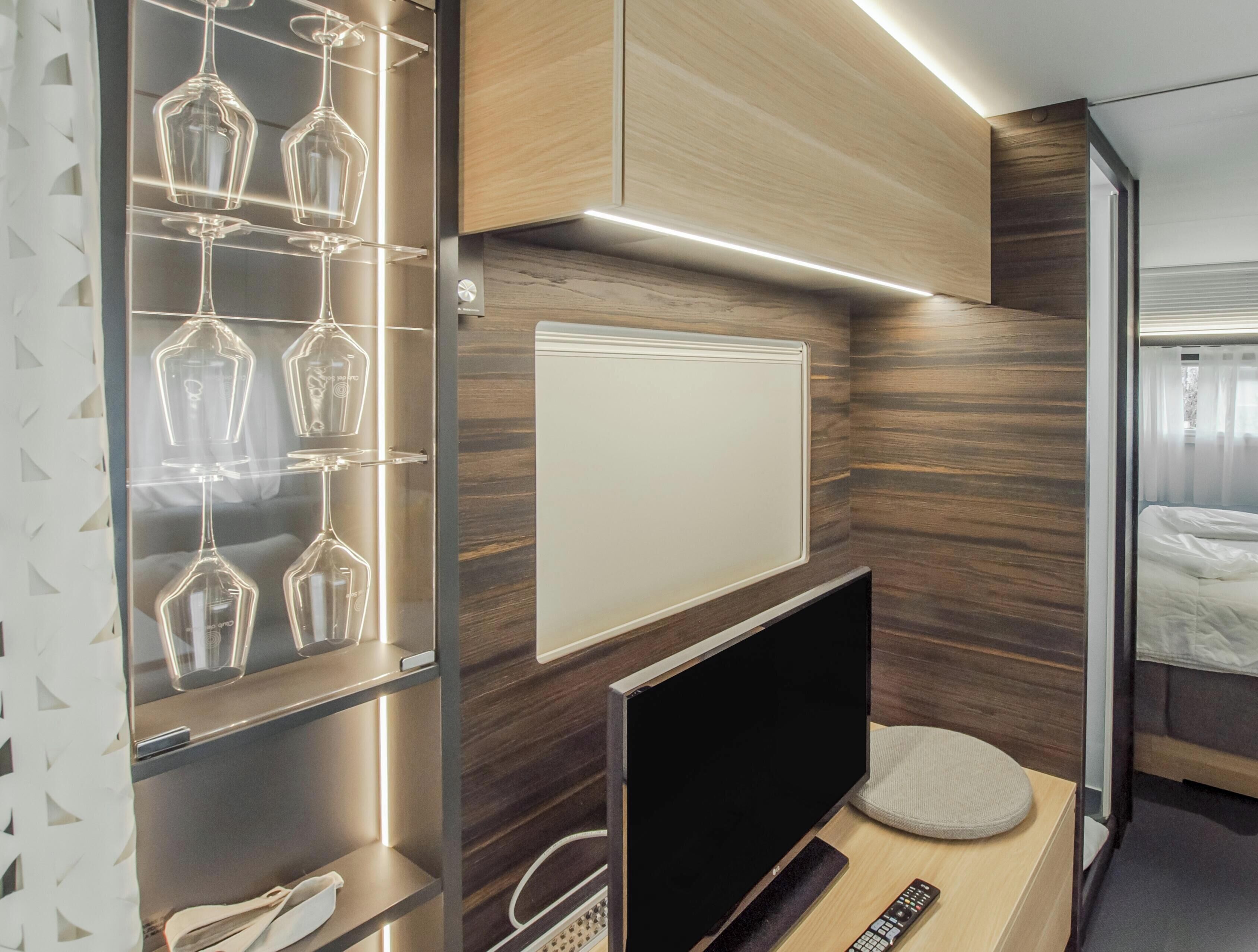 A compact room with a bed, a television, and a shelf with wine glasses.