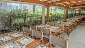 Un restaurante con mesas y sillas de madera, menús y vistas a la vegetación a través de amplias ventanas.