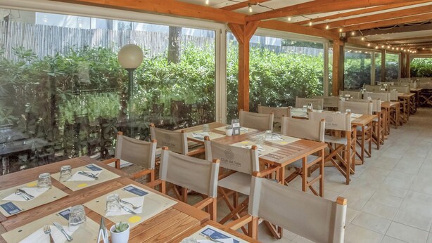 Ein Restaurant mit Holztischen und -stühlen, Speisekarten und Blick auf Grünanlagen durch große Fenster.