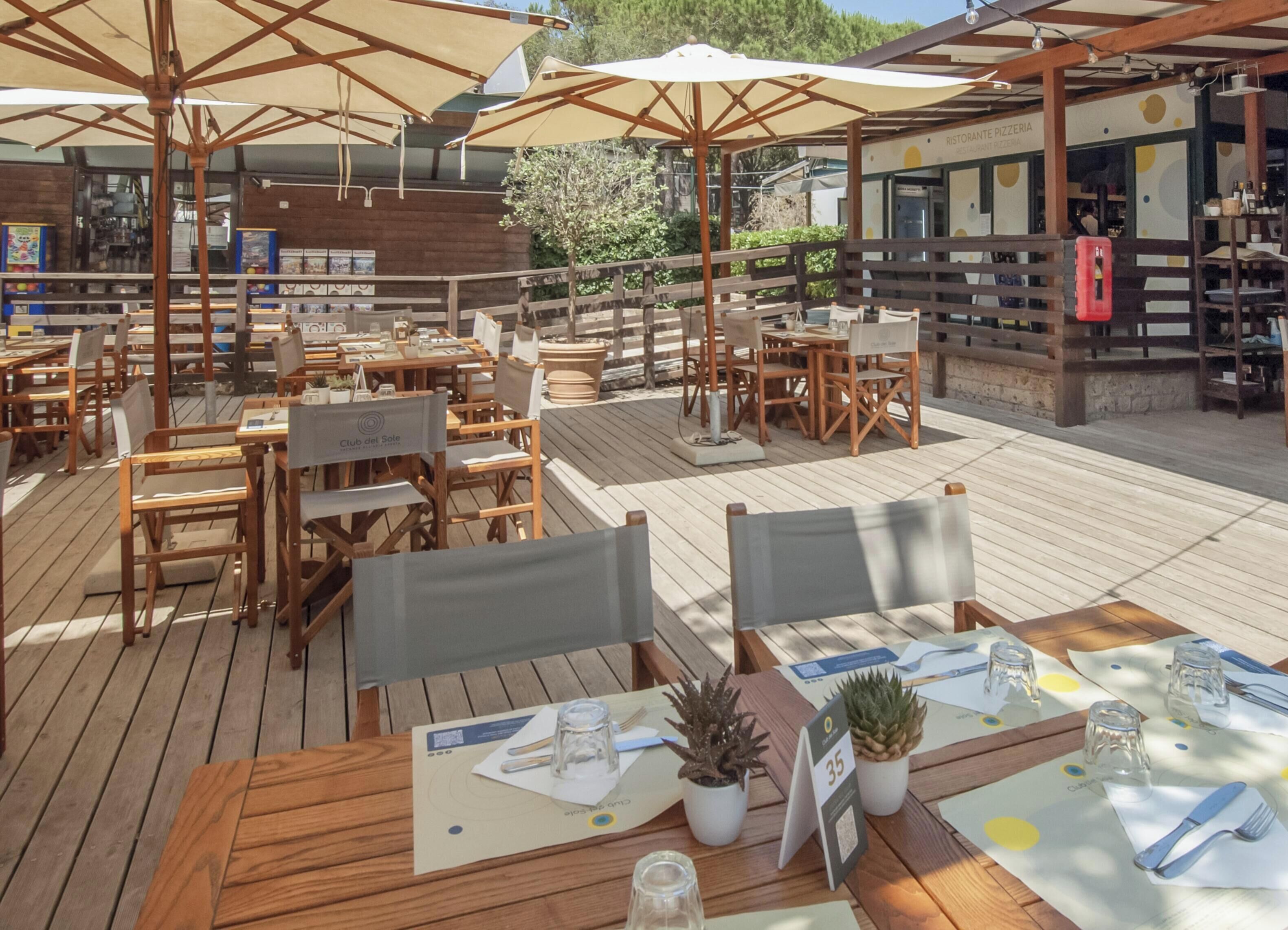 Un espace extérieur aménagé pour les repas, avec des tables et des chaises en bois, des parasols et des plantes en pot.