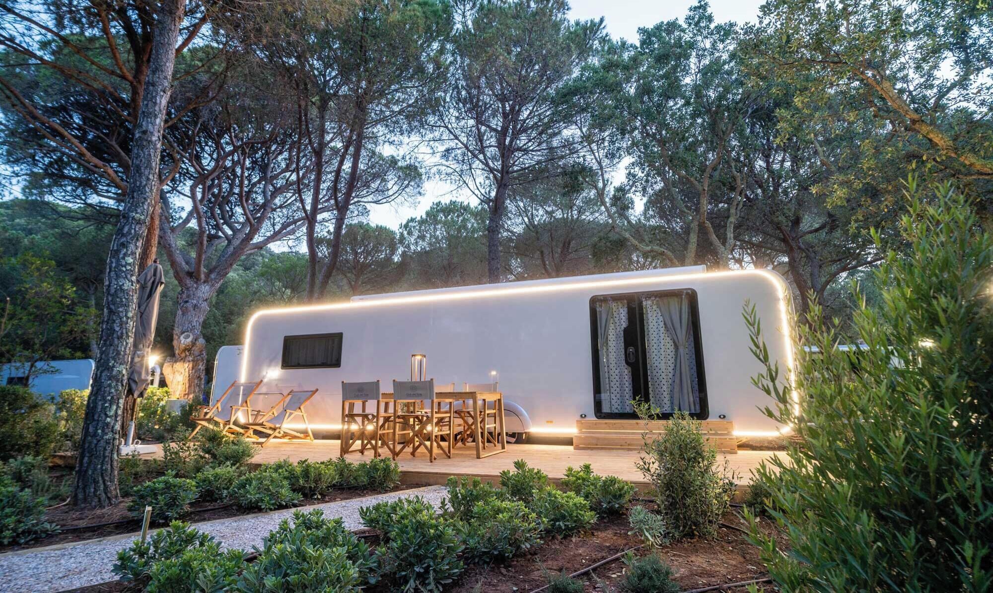 Una caravana moderna con porche cubierto, zona de estar exterior y jardín.