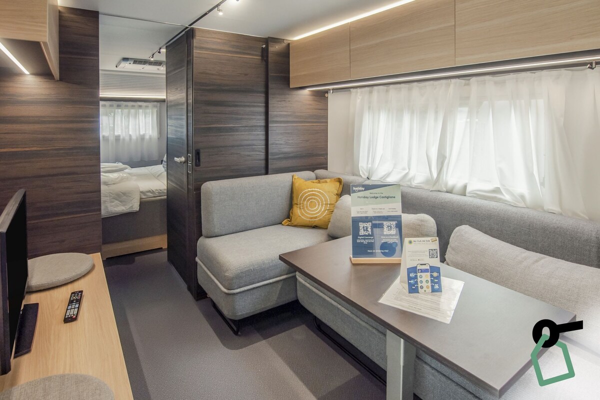 A compact, modern RV interior with a sofa, a small table with a brochure, and a TV.