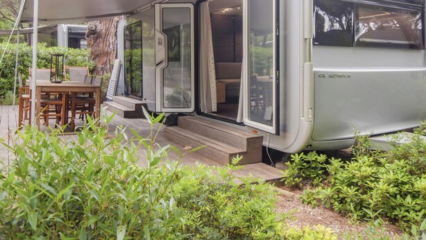 A mobile home with a covered patio area, a dining table, and a set of steps leading to the entrance.