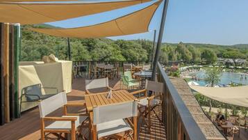 Terraza de madera con mobiliario exterior y vistas a una piscina y colinas.