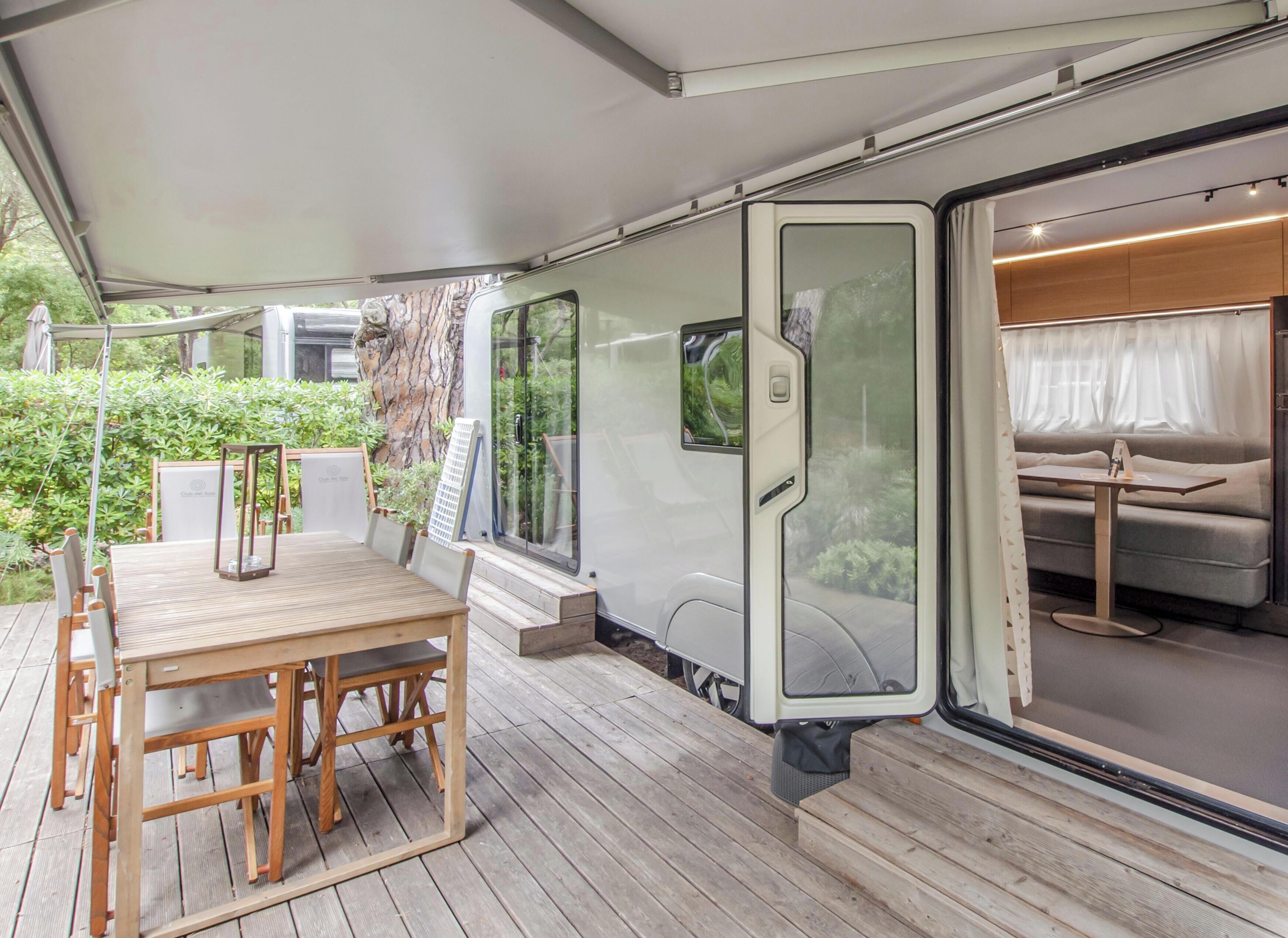 Un espacio al aire libre cubierto con una mesa y sillas de madera, un banco y vistas del interior a través de una puerta de cristal.