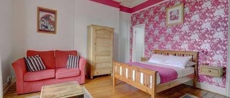 A bedroom with a wooden bed, a red sofa, a wooden chest of drawers, and a chandelier.