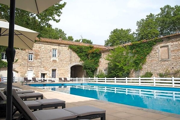 A stone building with a swimming pool, white fence, and lounge chairs.
