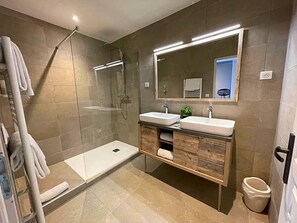 A modern bathroom with a glass shower enclosure, two sinks, a large mirror, and a towel rack.