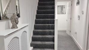 A staircase with a white handrail and a grey carpeted floor leading to a door. - London Oasis Modern 2BR Apartment (London)