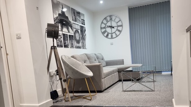 A modern living room with a grey sofa, a glass coffee table, and a large wall clock. - London Oasis Modern 2BR Apartment (London)
