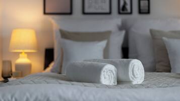 A neatly made bed with rolled white towels, a bedside lamp, and framed pictures on the wall.