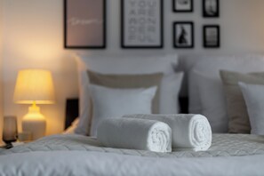 Una cama bien tendida, toallas blancas enrolladas, una lámpara de noche y cuadros en la pared.