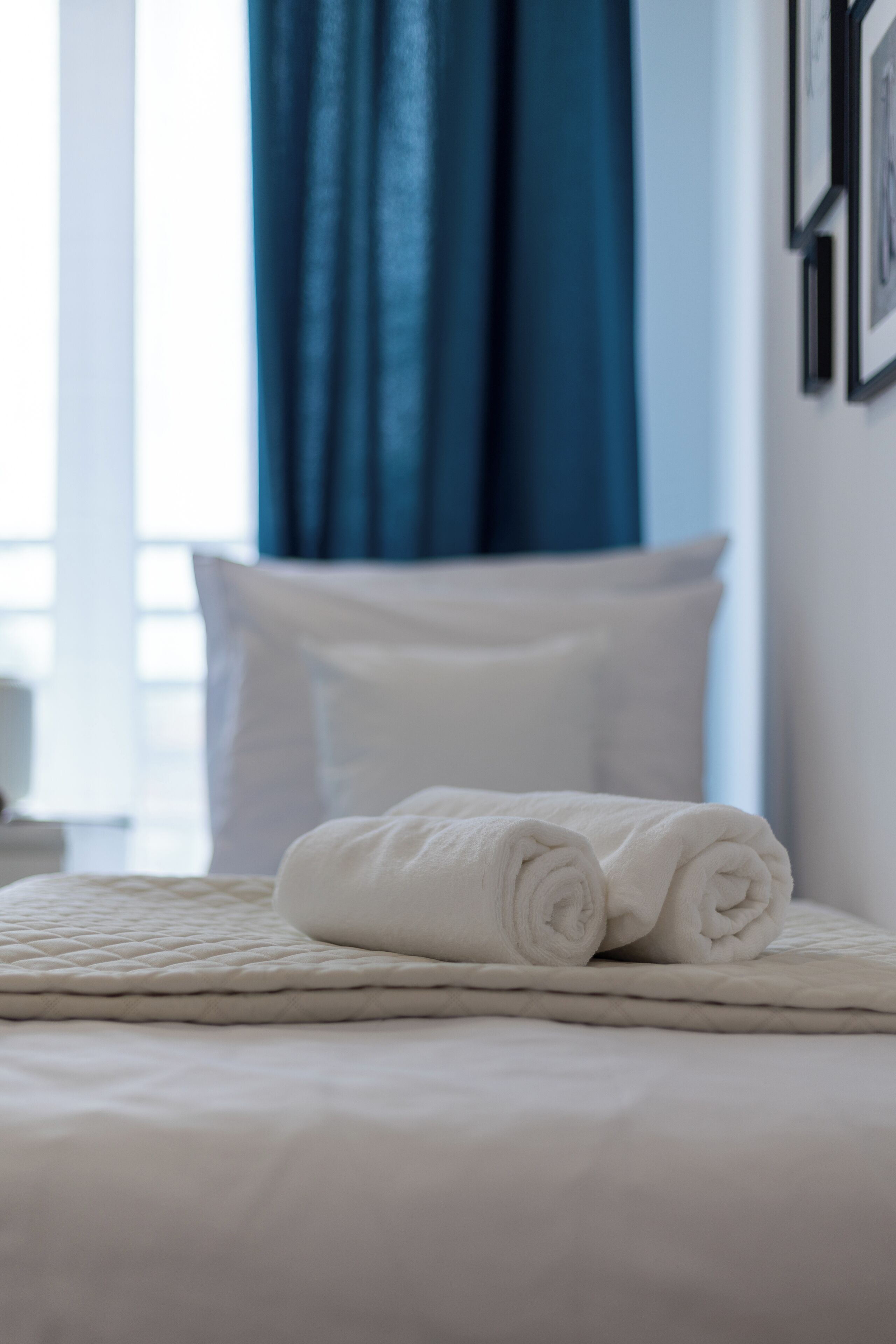 Een keurig opgemaakt bed met een opgerolde witte handdoek, witte kussens en een gewatteerde deken.